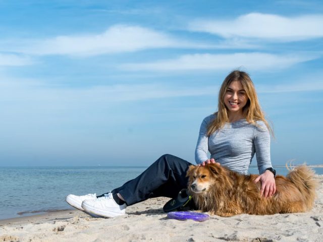 Woman enjoying a sunny day on Kołobrzeg beach with her dog, capturing the essence of leisure and companionship.
