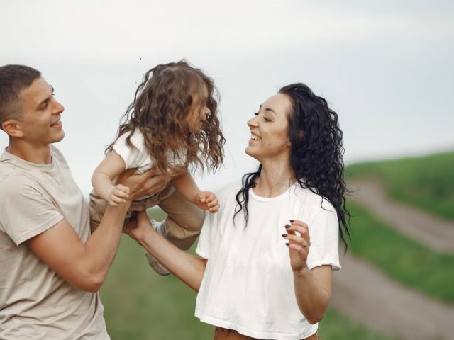 A joyful family moment outdoors with parents playing with their daughter.